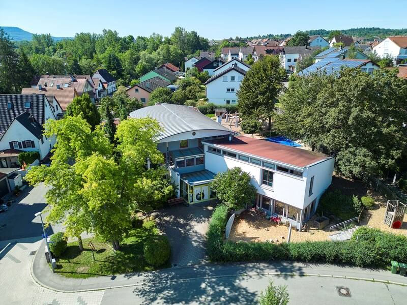 Ein modernes Gebäude umgeben von Bäumen und Vegetation, mit Straßenschildern und einem Gehweg im Vordergrund.