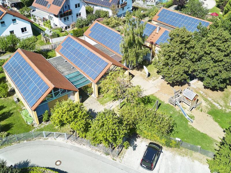 In einem Wohngebiet der Kindergarten, der mit Solarpanelen bedeckt ist, umgeben von grünen Bäumen und Gärten.
