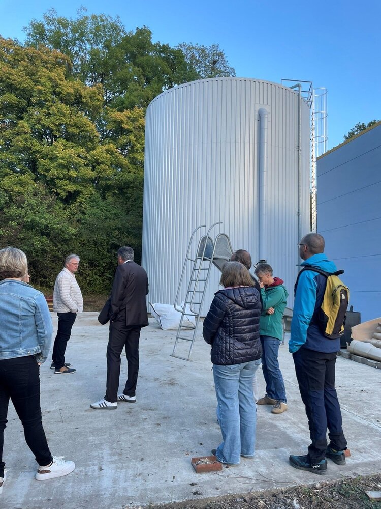 Eine Gruppe von Menschen steht draußen vor einem großen, metallernen Silotank.