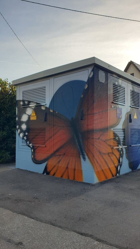 Ein großer orange-schwarzer Schmetterling ist auf einem Stromkasten an einer Straßenecke kunstvoll gemalt.