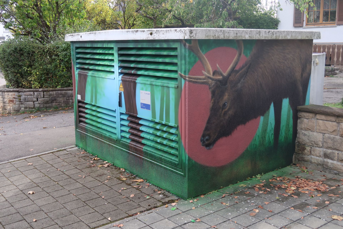 Auf einem Transformatorhäuschen ist ein realistisches Graffiti eines Hirschkopfes vor einem rosa Hintergrund zu sehen.