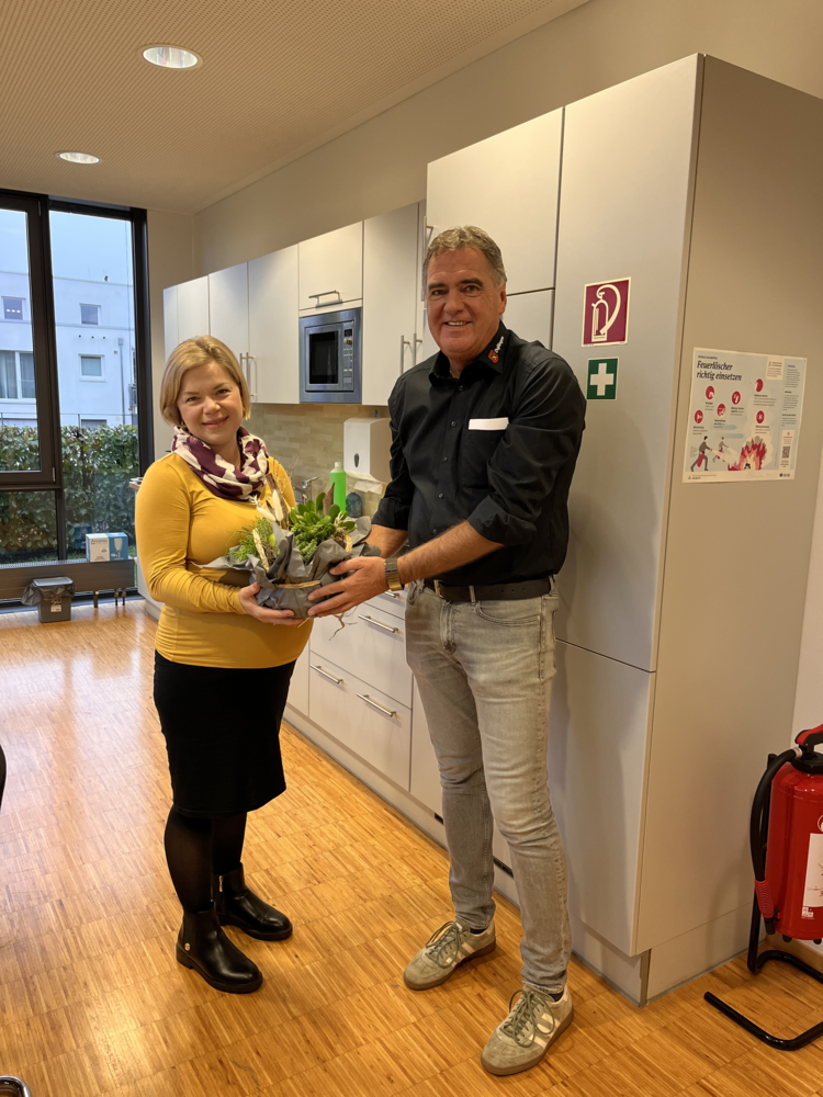 Ein Mann und eine Frau stehen in einer Küche, während sie gemeinsam einen kleinen Pflanzkübel halten.