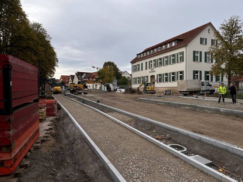 Eine Baustelle vor einem Gebäude mit der Aufschrift "Rathaus", umgeben von Erdarbeiten und Baumaschinen.