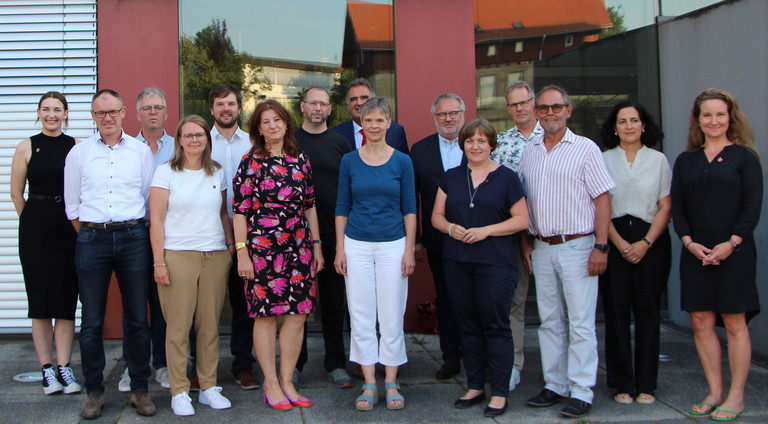 Eine Gruppe von 14 Personen steht vor einem Gebäude und lächelt in die Kamera.